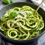 A bowl of vibrant zucchini noodles coated in basil pesto and topped with grated Parmesan cheese.