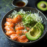 Keto salmon sashimi bowl with avocado, sesame seeds, and nori on a dark plate with wasabi and soy sauce on the side.