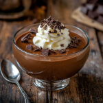 A glass bowl of keto pudding with chocolate shavings and whipped cream