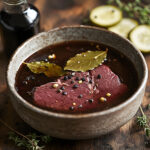 Beef steak marinating in dark pickle-based marinade with garlic and bay leaves